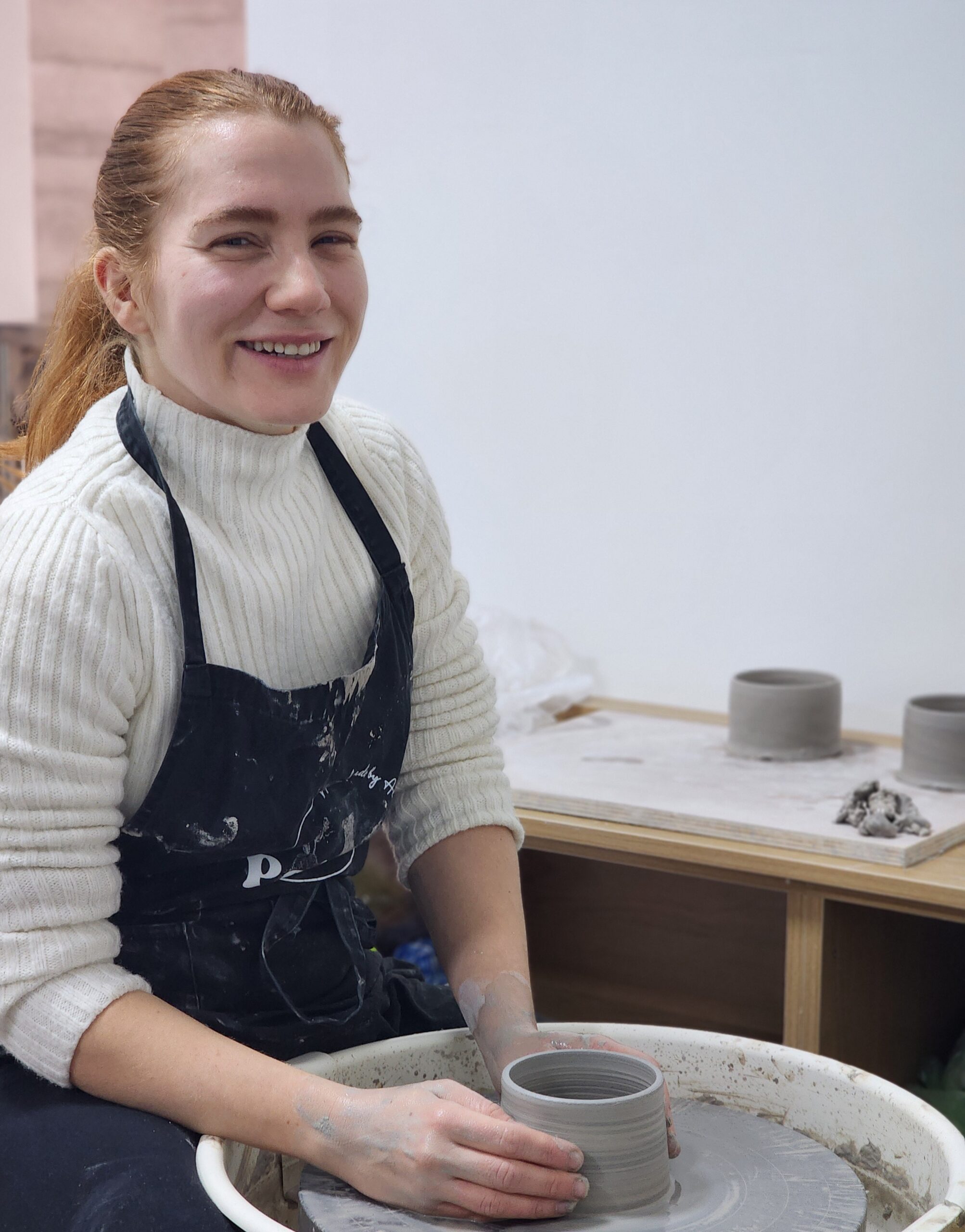 Potter shaping clay on a wheel in a sunlit studio